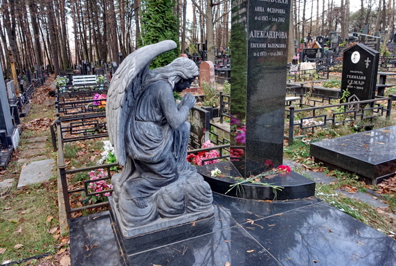 Статуя скорбящего ангела рядом с вертикальной стелой